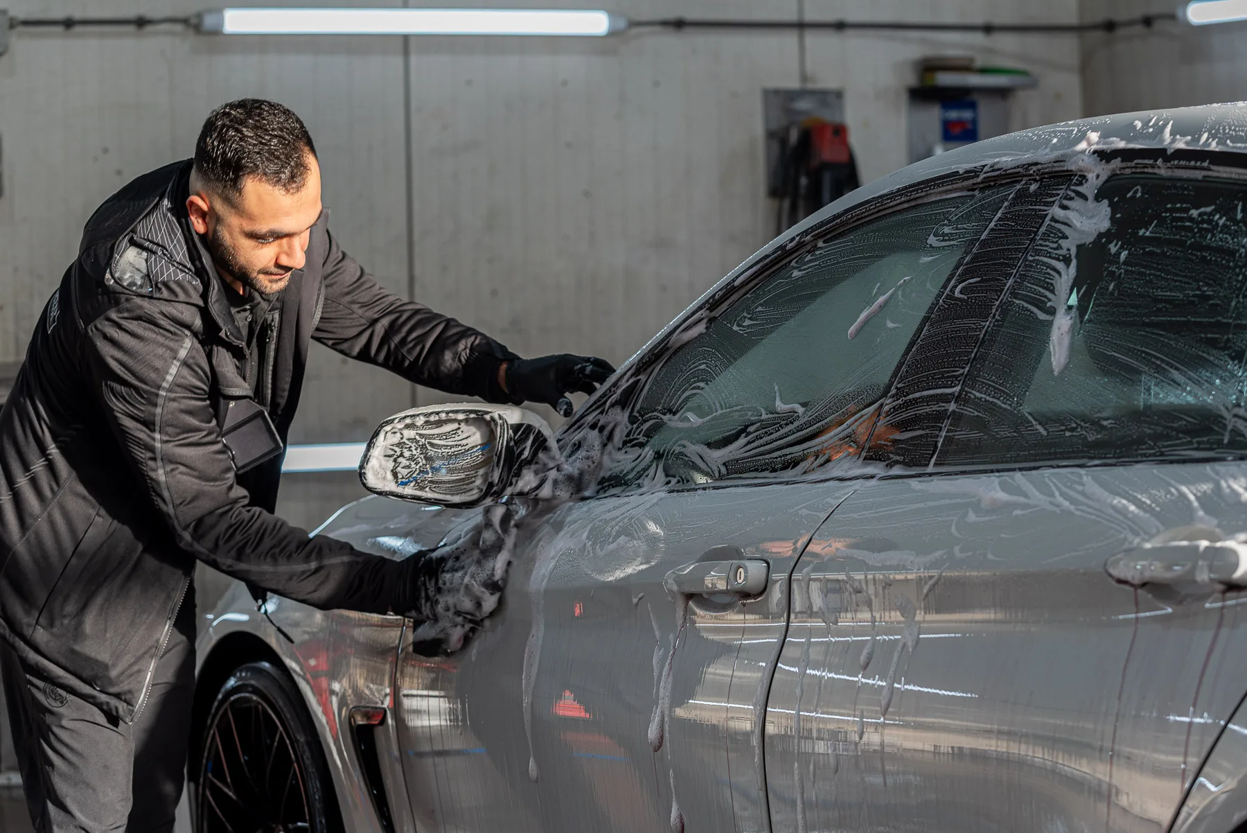 Een medewerker wast de zijkant van een grijze auto bij CLB Automotive